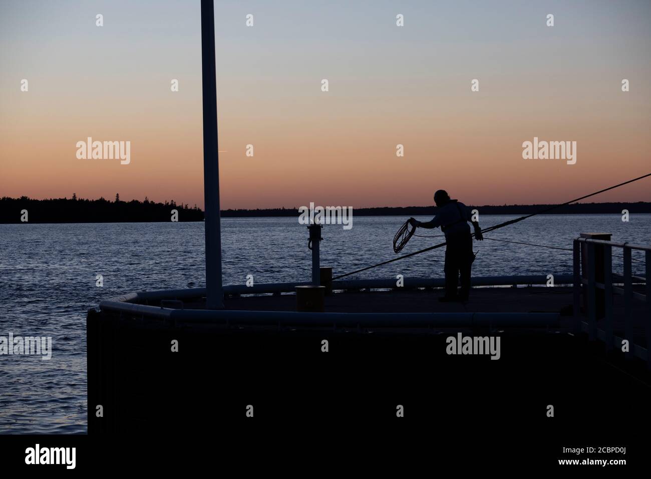 Silhouette di una persona che si avvolge la corda al tramonto Un molo a Tobermory Foto Stock