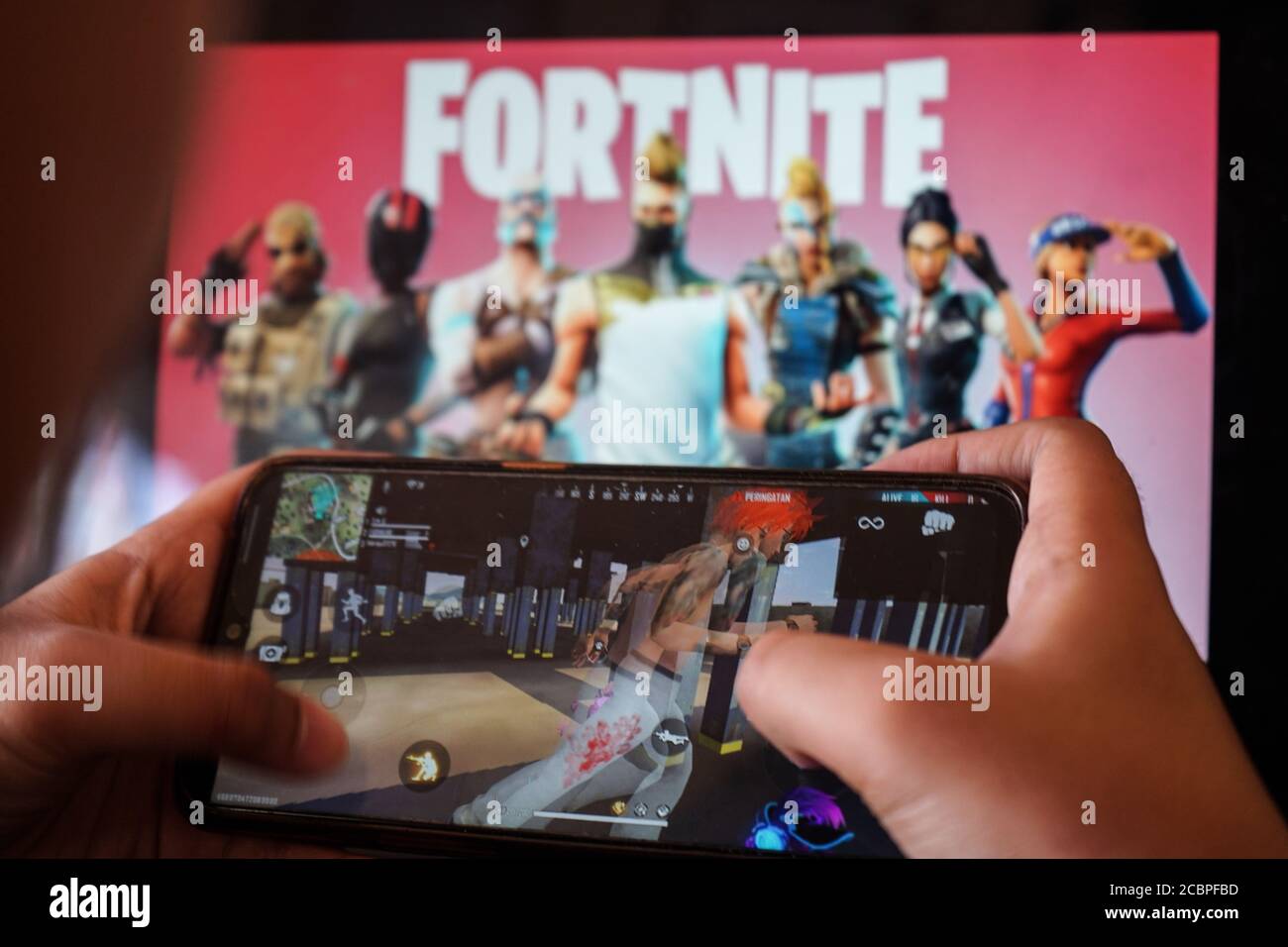 Makassar, Sulawesi del Sud, Indonesia. 15 agosto 2020. Un bambino sta  giocando un gioco su un cellulare con un'immagine del gioco Fortnite sullo  schermo del computer in background. Apple e Google hanno