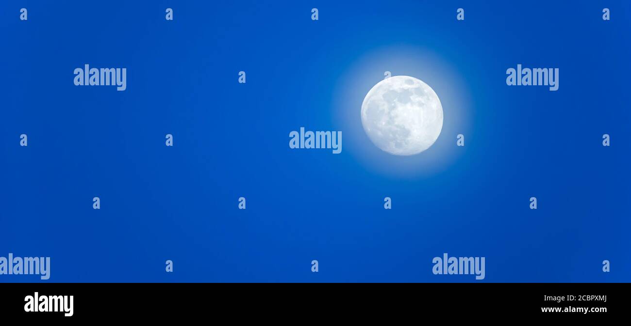La luna piena splende nella nebbia mattutina sul cielo blu. Foto Stock