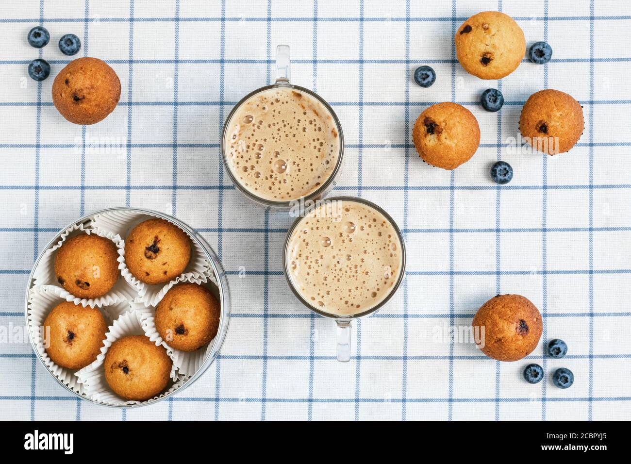 Due tazze di caffè e muffin al mirtillo su una tovaglia a scacchi. Concetto di colazione. Design piatto. Cibo sfondo, carta da parati Foto Stock
