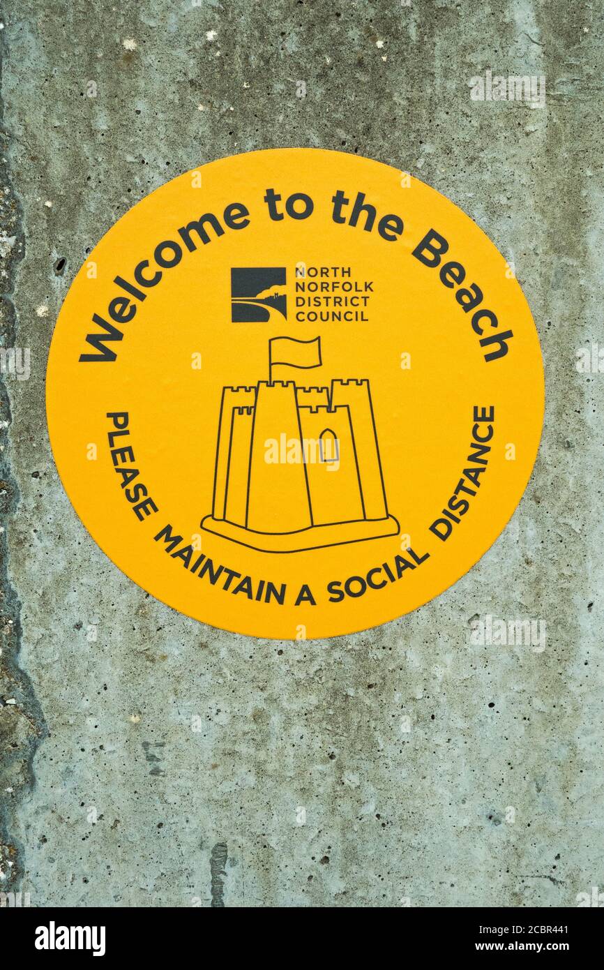 'Benvenuti in spiaggia, si prega di mantenere una distanza sociale' adesivo giallo per North Norfolk District Council, Sheringham, Norfolk, Inghilterra Foto Stock