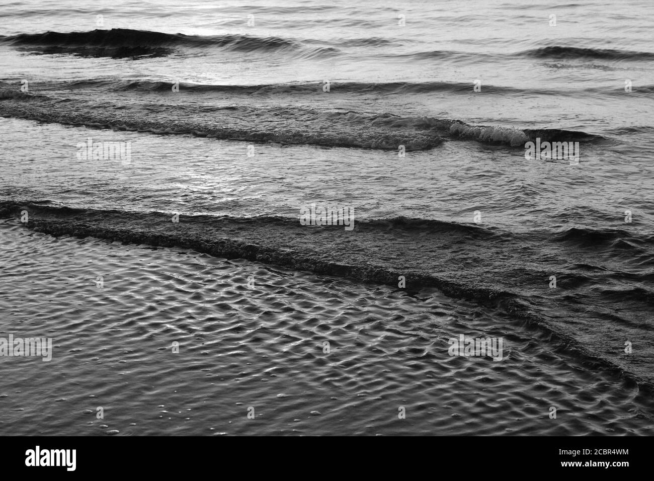 Sfondo bianco e nero raffigurante piccole onde che arrivano al costa di un oceano Foto Stock