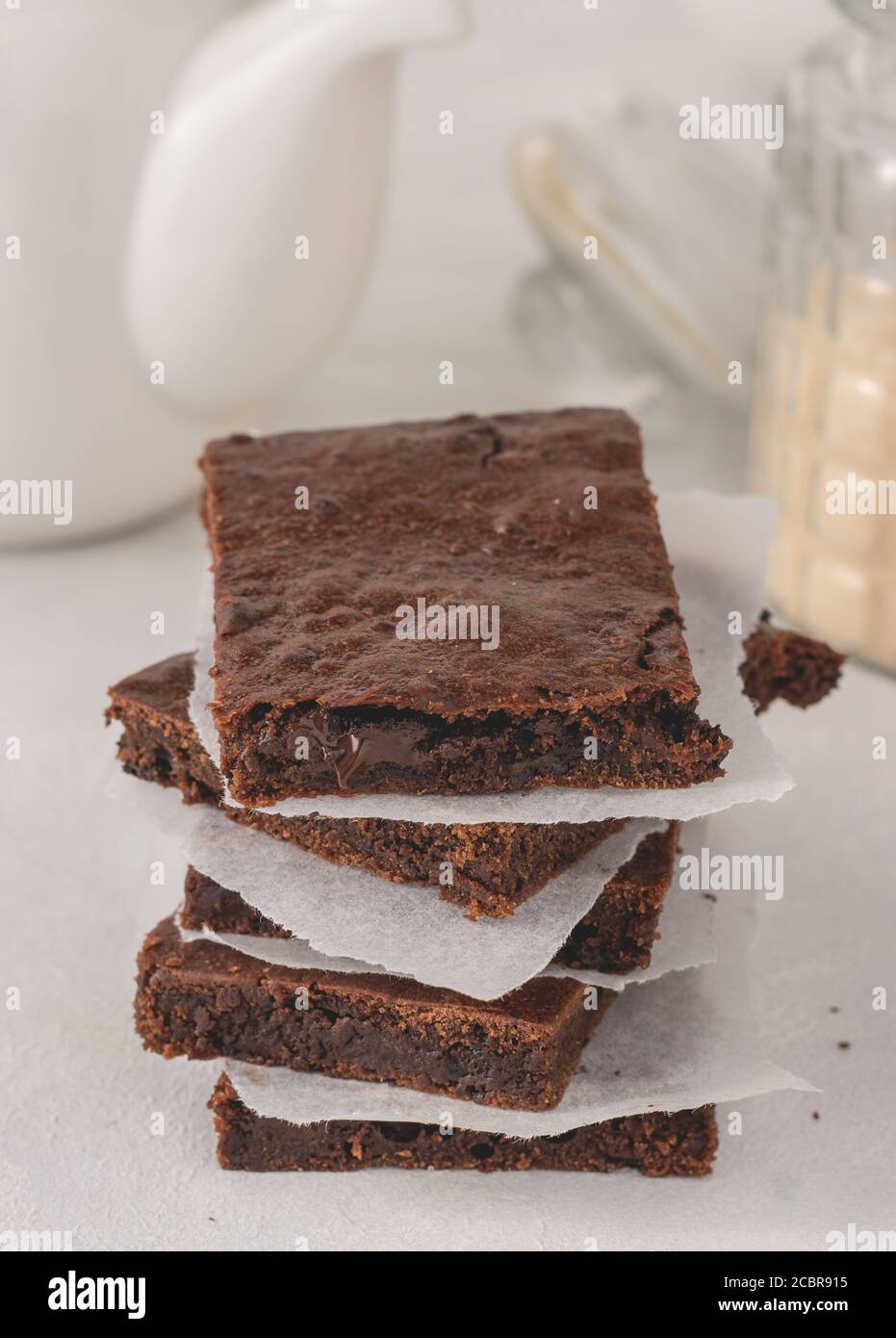 Una pila di brownie di cioccolato con carta pergamena tra posto su sfondo bianco. Delizioso dessert. Foto Stock