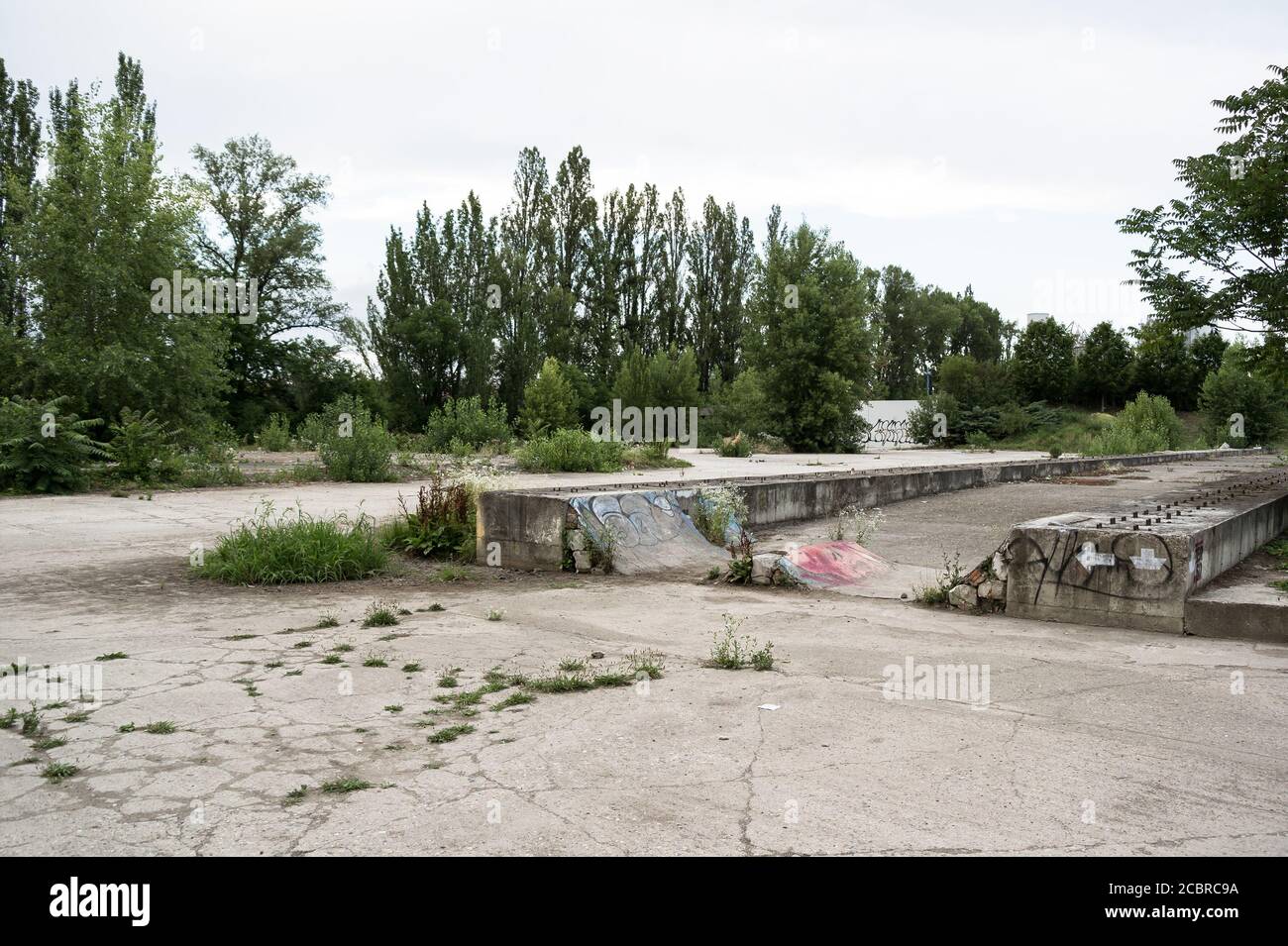 Isola di Rohan, Praga, Repubblica Ceca / Czechia - luogo abbandonato con superficie in cemento. L'area è ricoperta di erba e vegetazione. Graffiti e skae Foto Stock