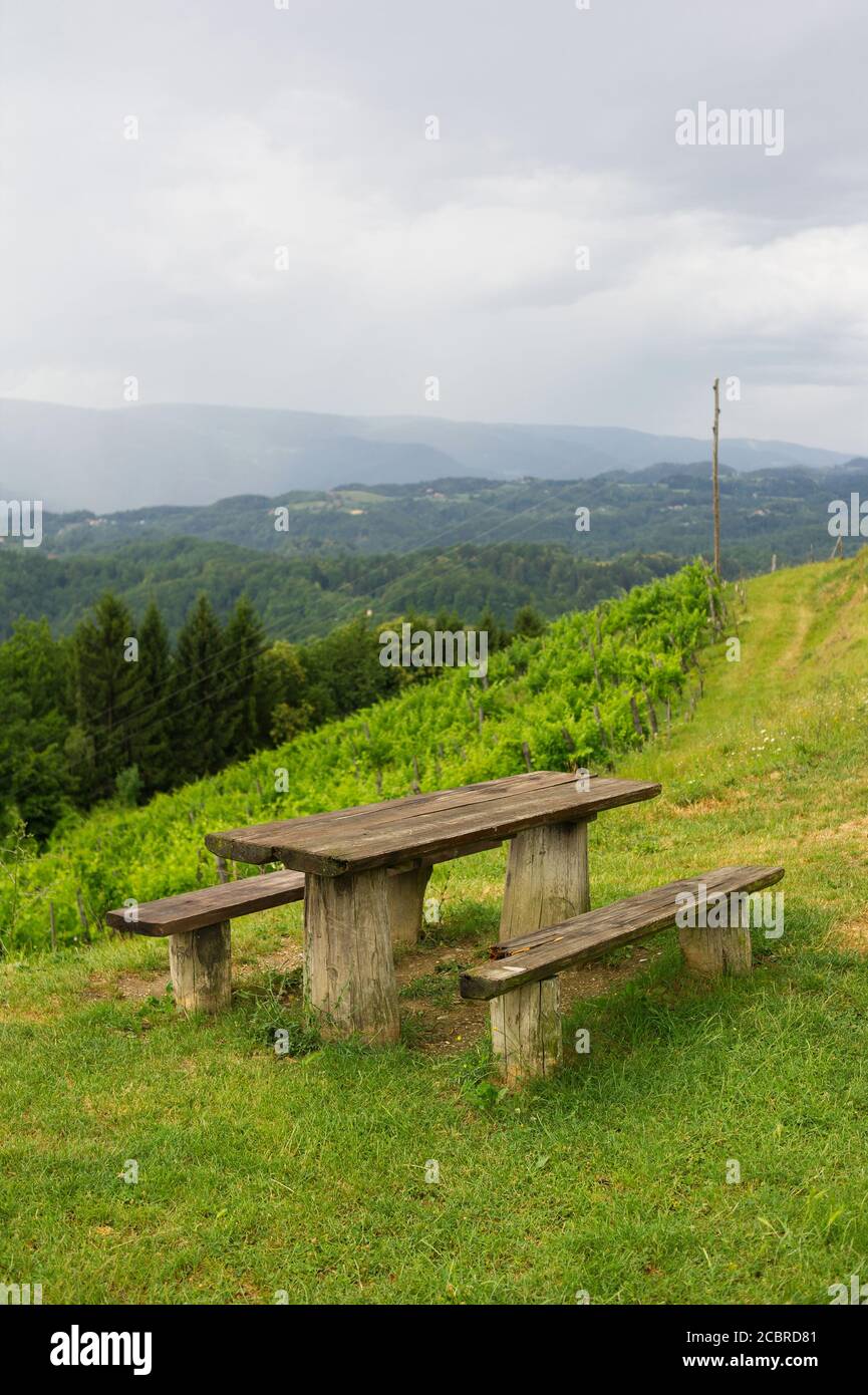 Sveti Urban, vicino a Maribor, Slovenia - panca rustica in legno, tavolo e bella natura della campagna slovena con vigneto. Tempo eccessivo Foto Stock