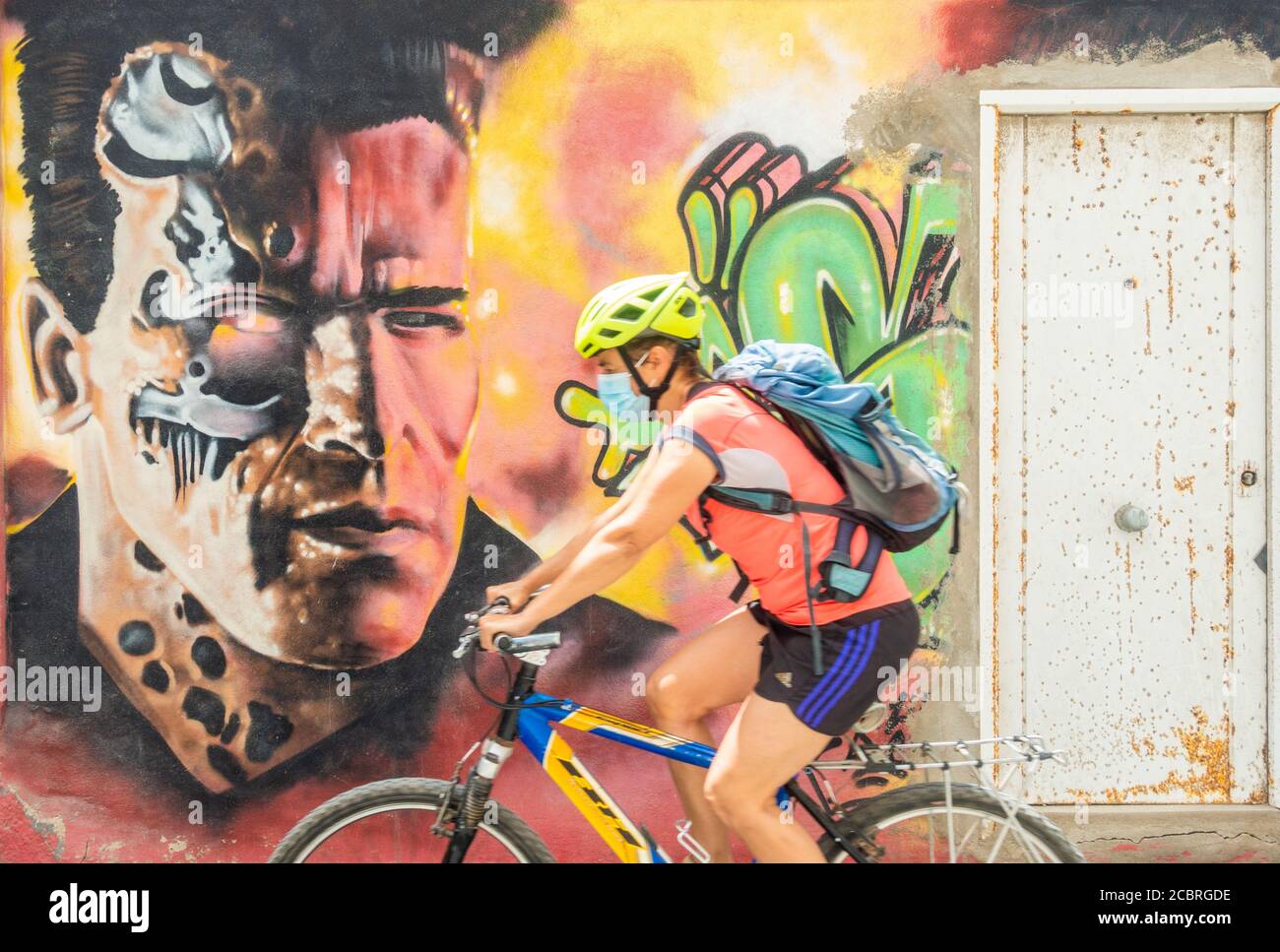 Las Palmas, Gran Canaria, Isole Canarie, Spagna. 15 agosto 2020. Una donna che indossa una maschera facciale passa i graffiti di Arnold Schwarzenegger/Terminator a Las Palmas su Gran Canaria, mentre il governo delle Canarie vieta di fumare all'aperto e rende obbligatoria la maschera facciale all'aperto (anche sulle spiagge se non è in grado di rispettare le distanze sociali) nel tentativo di arginare l’attuale aumento dei nuovi casi di coronavirus. La maggior parte dei nuovi casi si trova in persone di età inferiore ai 30 anni. Credit: Alan Dawson/Alamy Live News Foto Stock