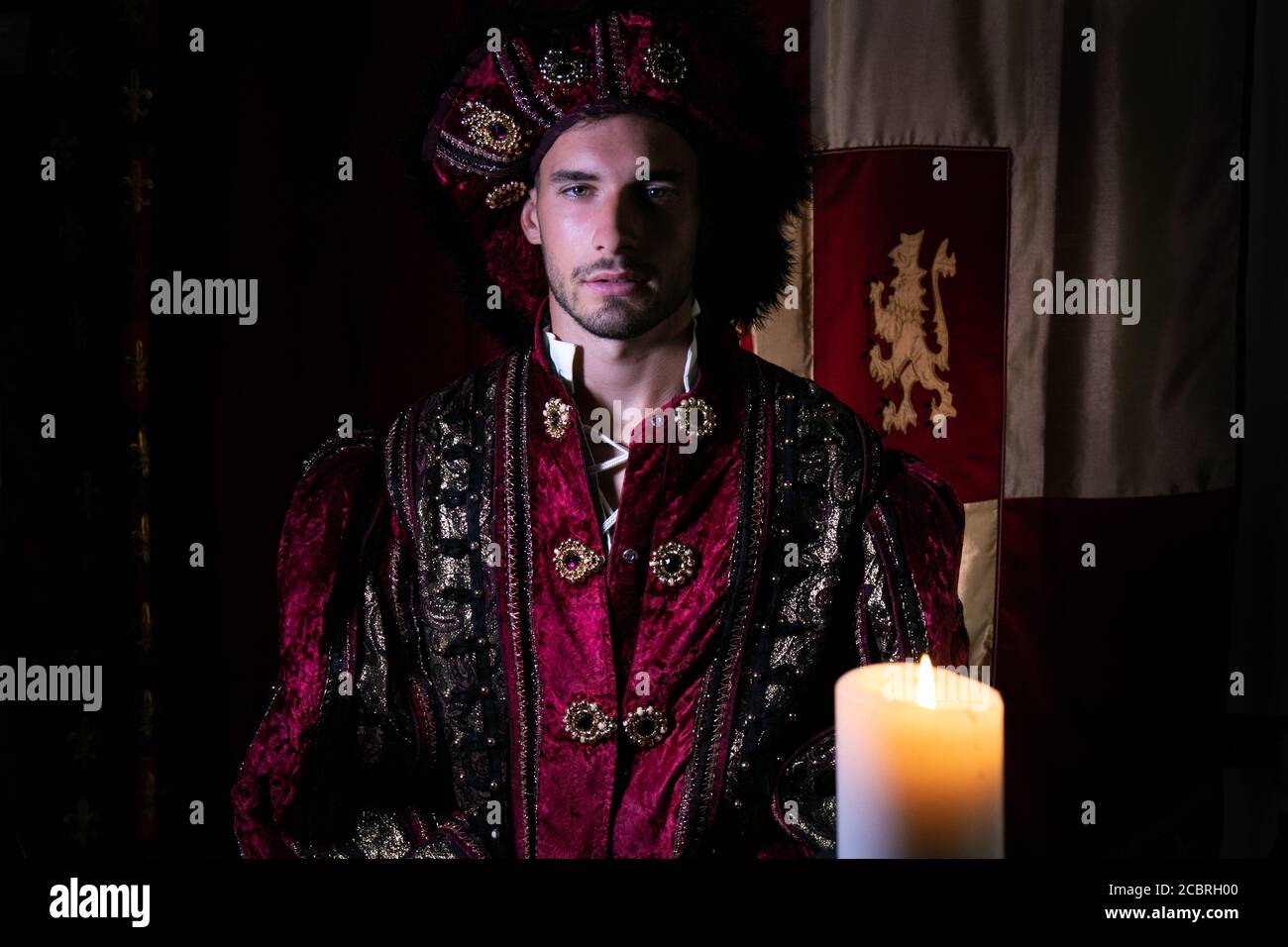 Ritratto di re attraente con barba vestita in costume alla macchina fotografica con la candela in primo piano Foto Stock