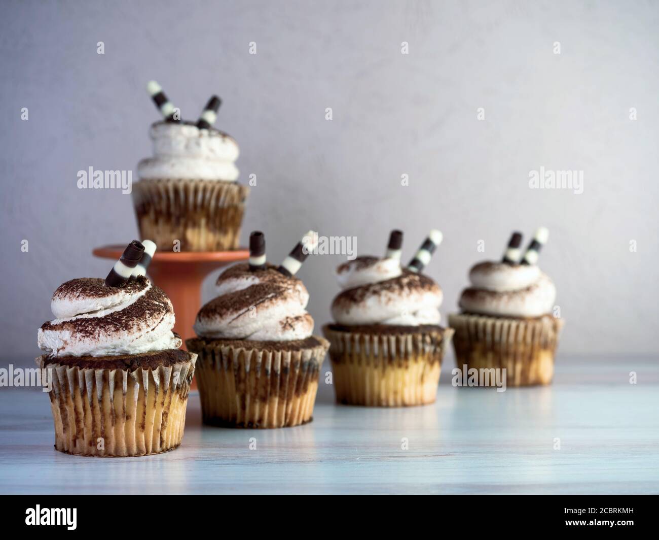 Tiramisù cupcakes allineati con bianco gelando impilato alto e. cospargere di polvere di espresso e cioccolato bianco e scuro bastone con un cuppak rialzato Foto Stock