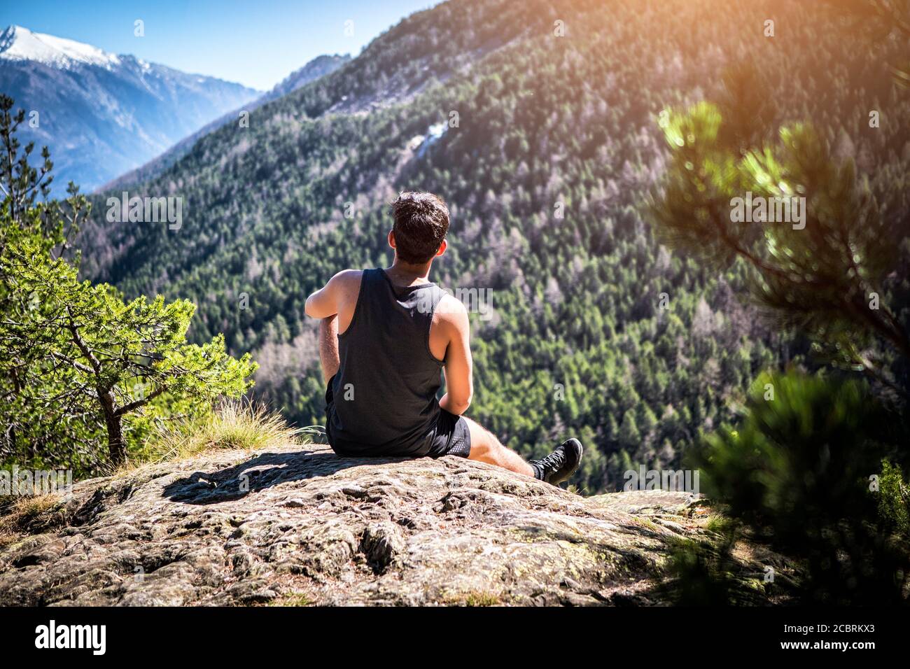 Giovane seduto su una roccia che gode di vista sulle montagne Foto Stock