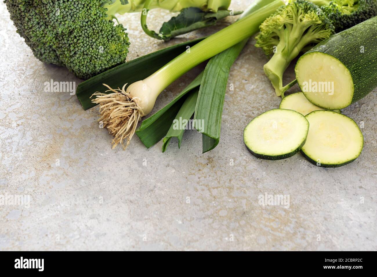 Verdure verdi sane come zucchine, porri e broccoli su uno sfondo grigio con spazio di copia, fuoco selezionato, profondità di campo stretta Foto Stock