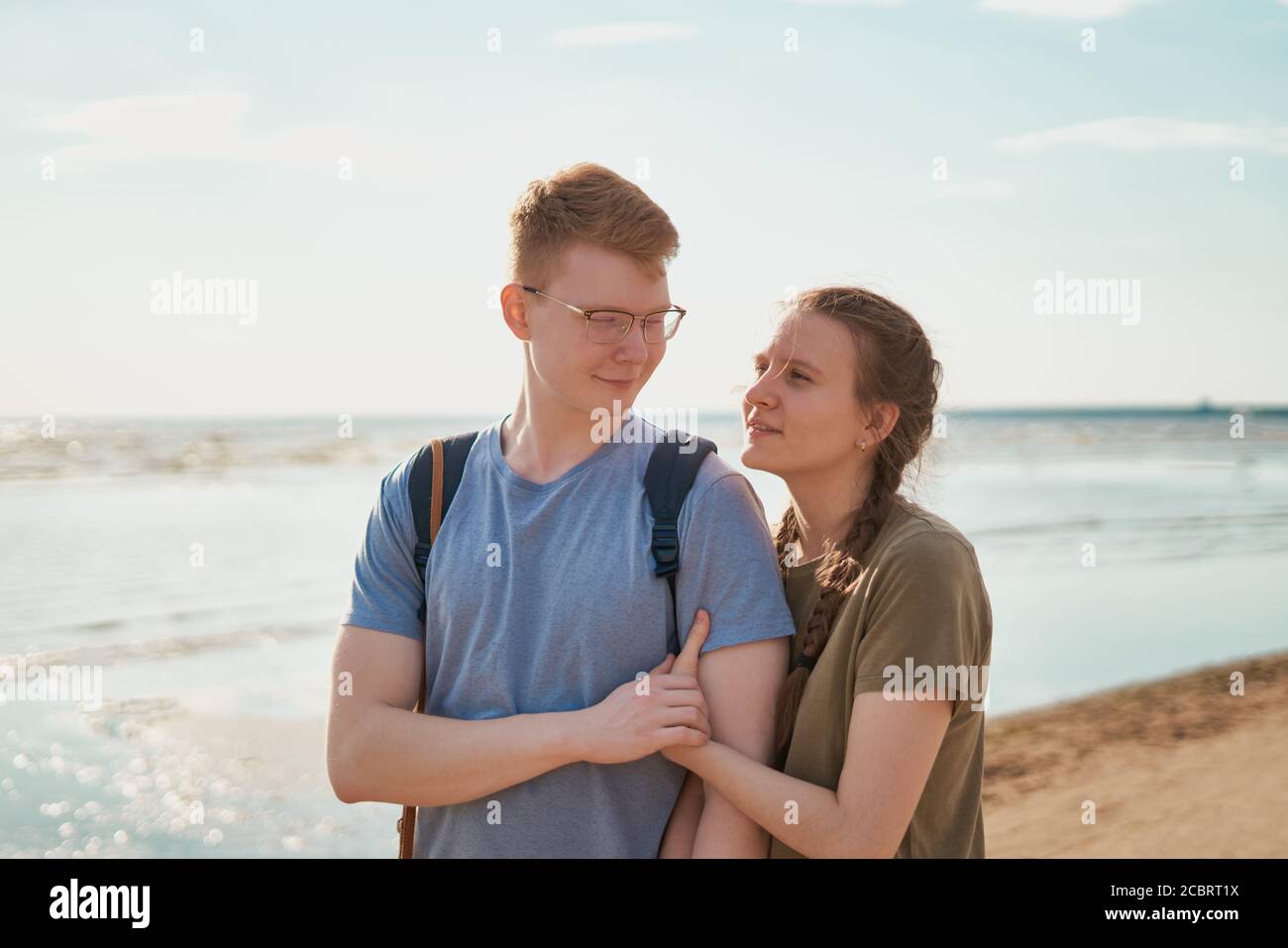 Millennial coppia abbracciando e posando sulla spiaggia in giornata di sole Foto Stock