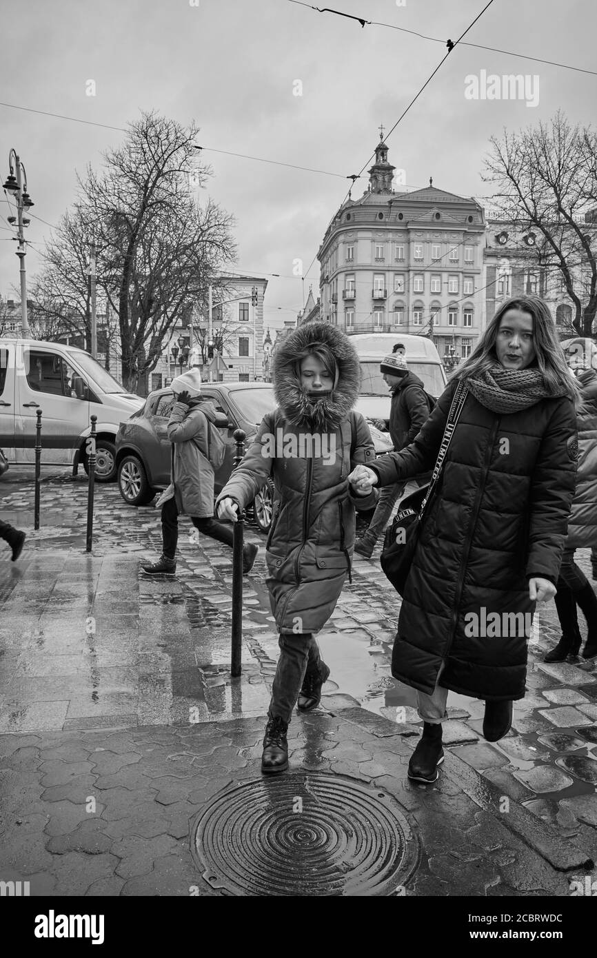 Le ragazze che tengono le mani camminano giù la strada. Lviv/Ucraina - 30 gennaio 2020: I passanti camminano sul marciapiede bagnato in via Petra Doroshenka. Foto Stock