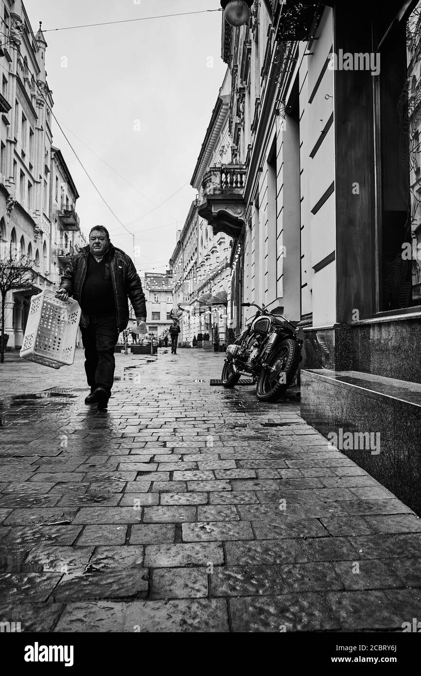 Strada, uomo, motocicletta parcheggiata. Lviv/Ucraina - 30 gennaio 2020: Un uomo penoso porta una scatola vuota lungo la via Les Kurbas. Foto Stock
