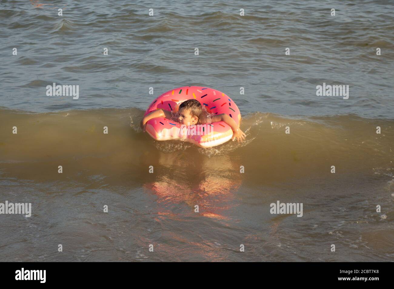 Un ragazzo di 5 anni nuota e si diverte in mare vicino alla riva con un cerchio gonfiabile a forma di ciambella. Foto Stock