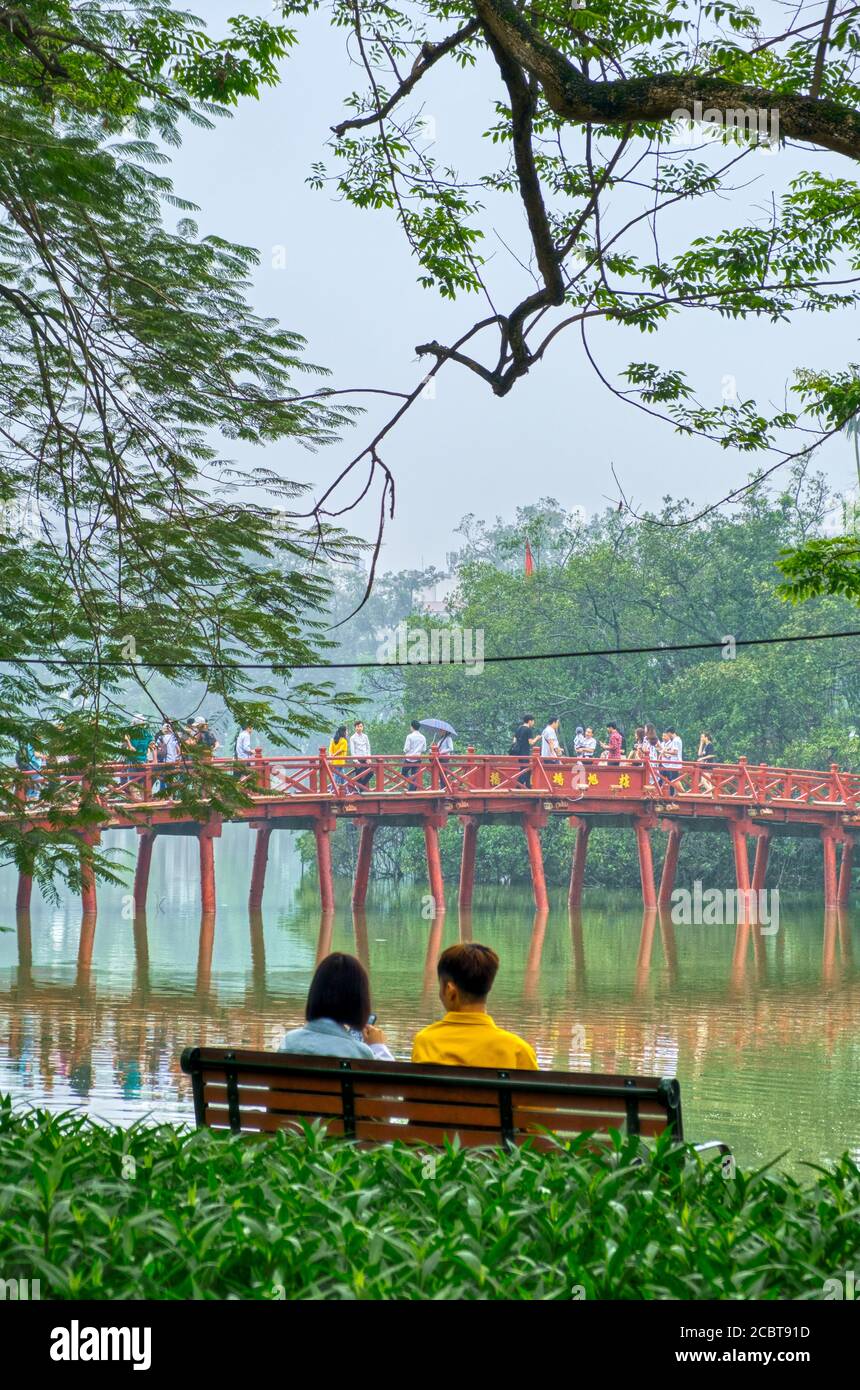 Lago Hoan Kiem, distretto di Hanoi Ba Dinh, Vietnam. Una coppia su una panchina rilassante, riflessione lago. Foto Stock