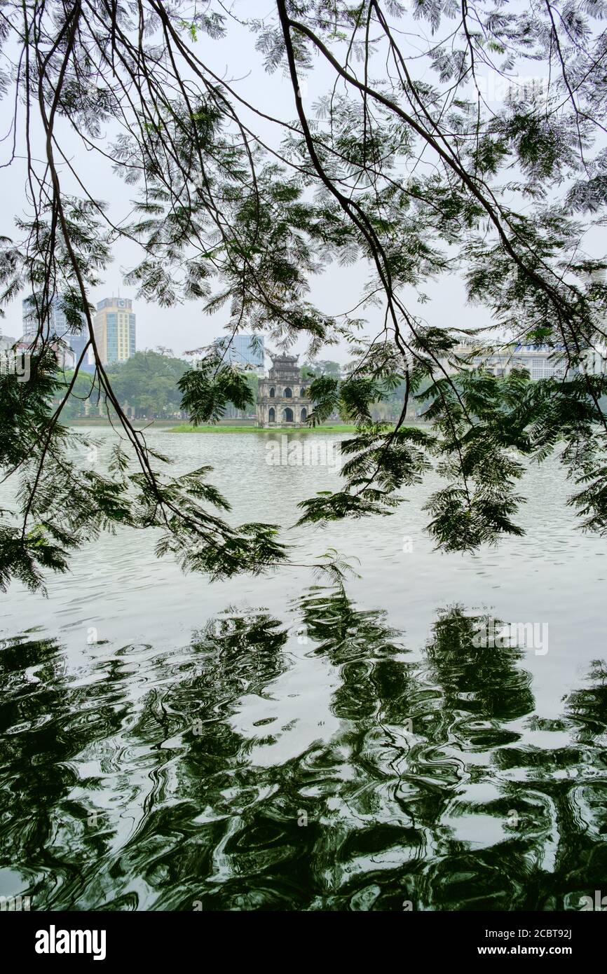 Hanoi, Vietnam, lago Hoan Kiem con la Torre delle tartarughe (pagoda) incorniciata tra le foglie. Riflessione in un'immagine HDR verticale. Hanoi luogo iconico. Foto Stock