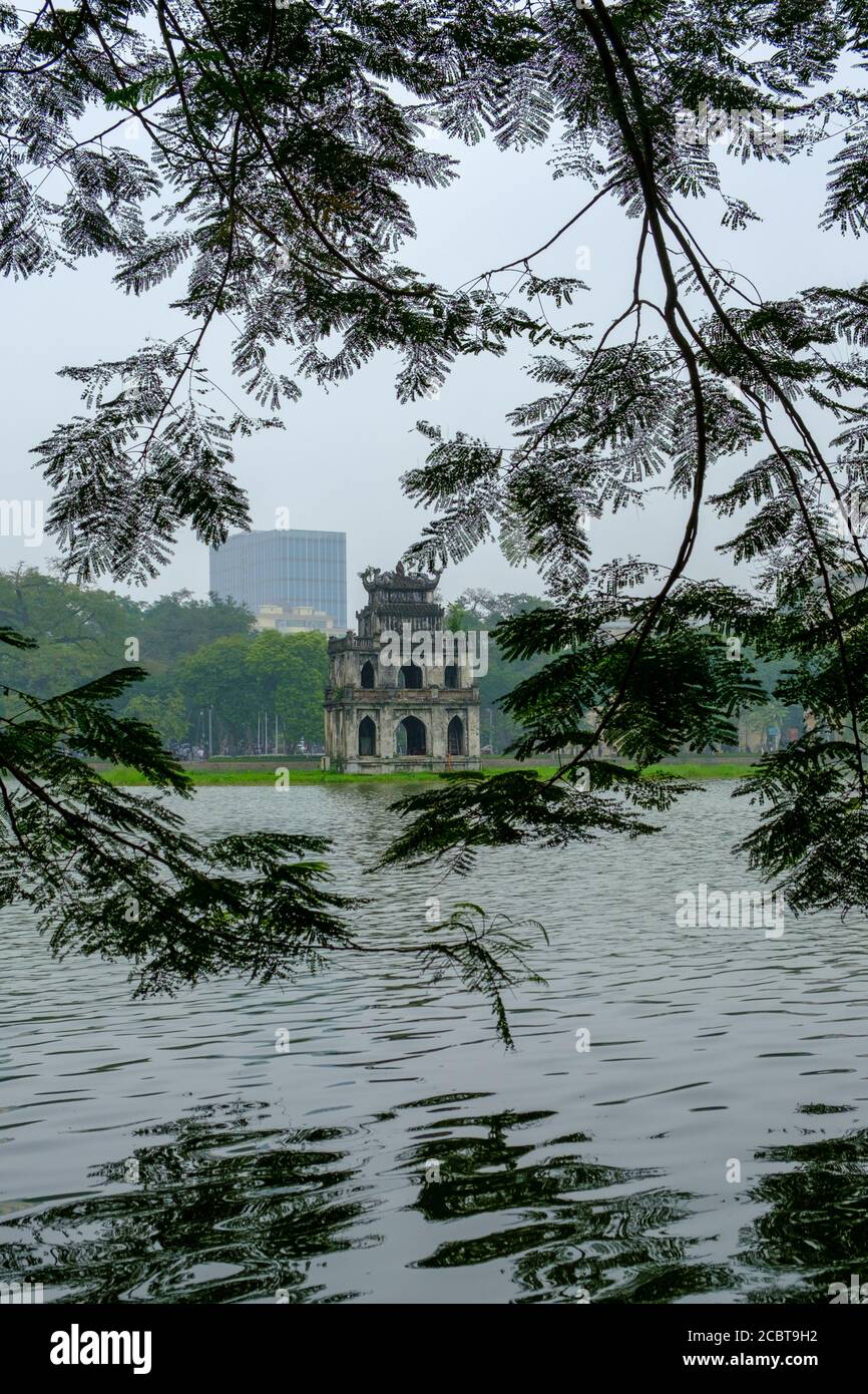 Hanoi, Vietnam, lago Hoan Kiem con la Torre delle tartarughe (pagoda) incorniciata tra le foglie. Riflessione in un'immagine HDR verticale. Foto Stock