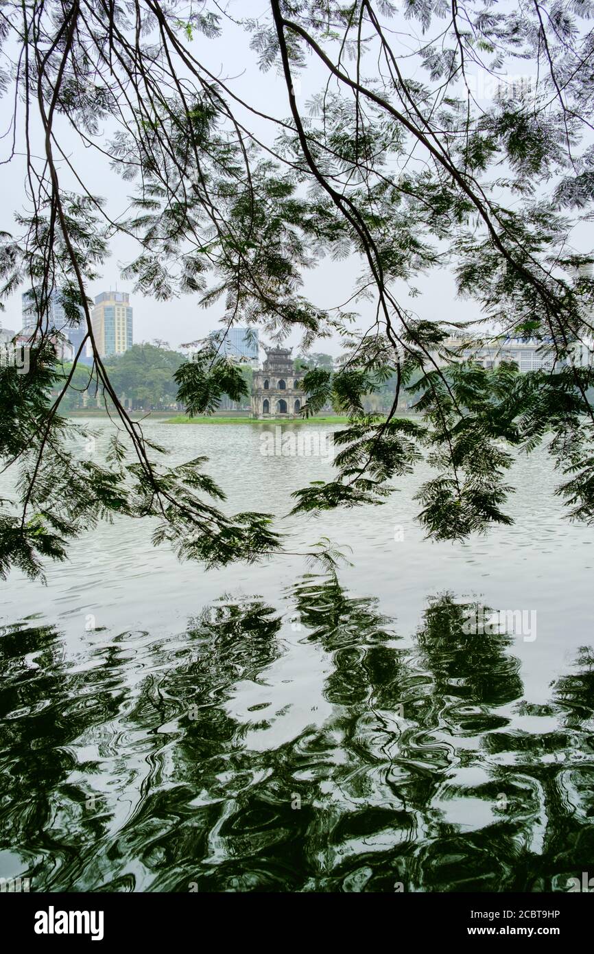 Hanoi, Vietnam, lago Hoan Kiem con la Torre delle tartarughe (pagoda) incorniciata tra le foglie. Riflessione in un'immagine HDR verticale. Foto Stock
