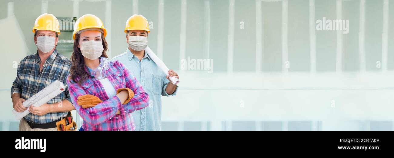 Appaltatori femminili e maschili in cappelli duri che indossano maschere mediche del viso al luogo di costruzione durante il banner pandemico di Coronavirus. Foto Stock