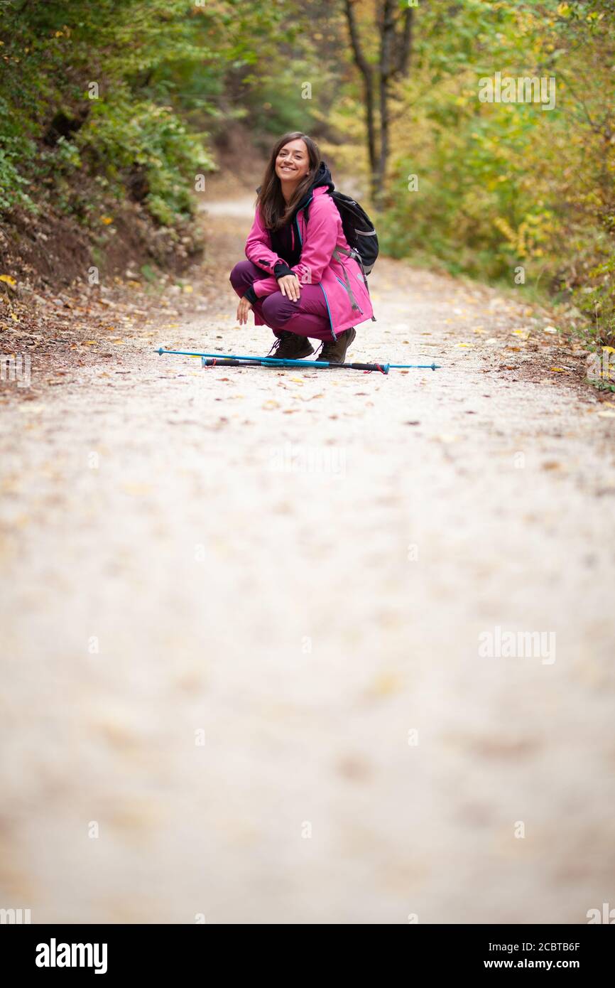 Ragazza escursionista accovacciata su un sentiero in montagna. Backpacker con giacca rosa in una foresta. Stile di vita sano all'aperto. Foto Stock