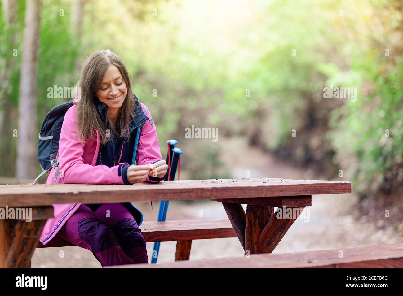 Ragazza escursionista che riposa su una panchina nella foresta. Zaino in spalla con giacca rosa che tiene foglie secche d'autunno. Foto Stock
