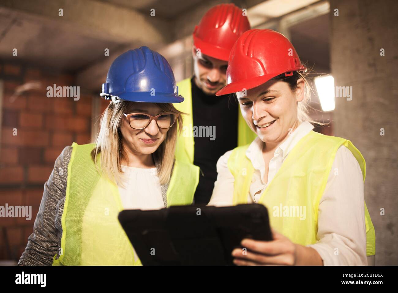 team di ingegneri in giubbotti e cappelli duri con un tablet, in un cantiere Foto Stock
