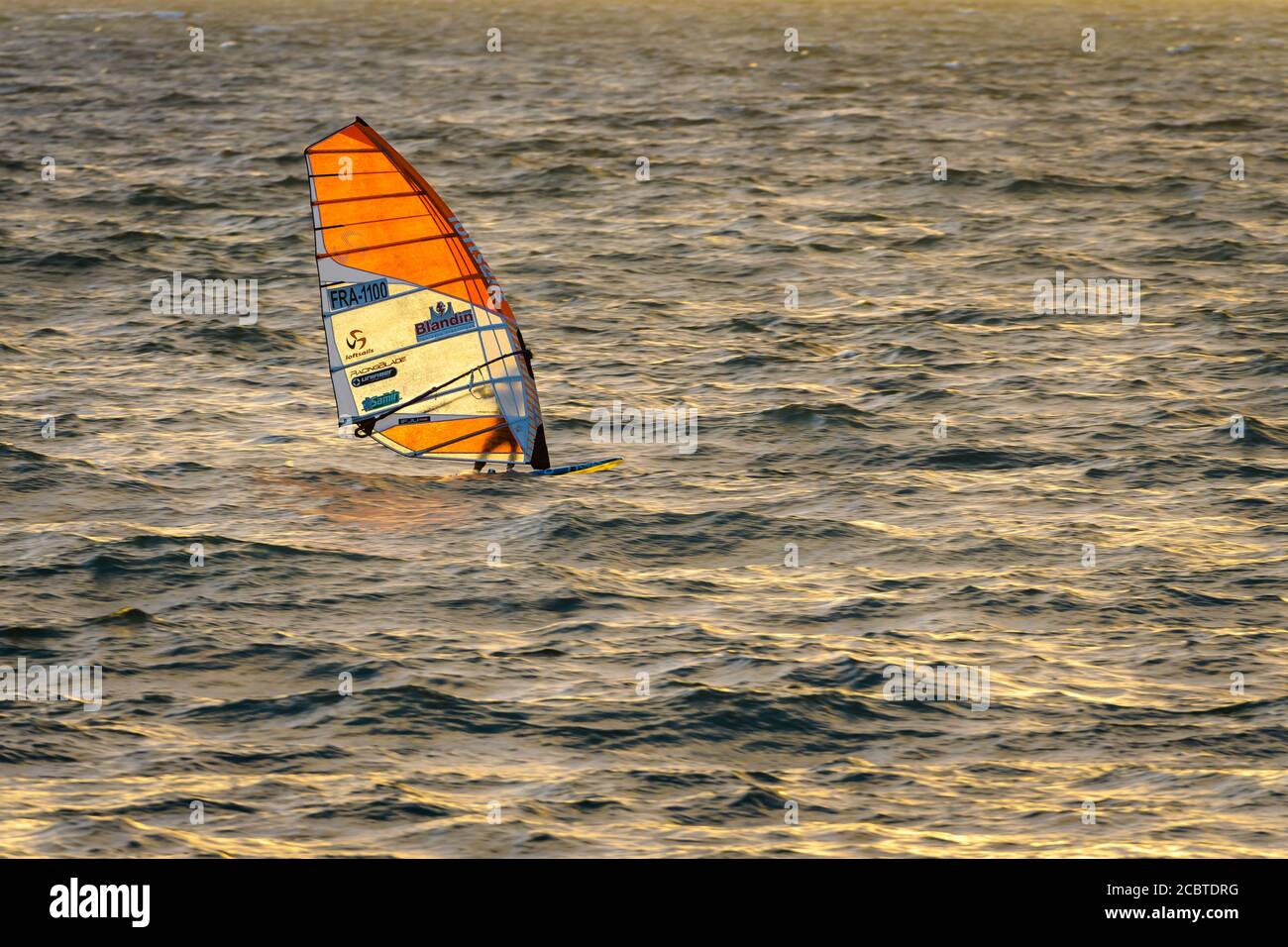 Tramonto d'oro sulla splendida spiaggia di Brighton ad Adelaide, Australia del Sud, mentre il suo windsurf si muove retroilluminato attraverso l'oceano meridionale. Foto Stock