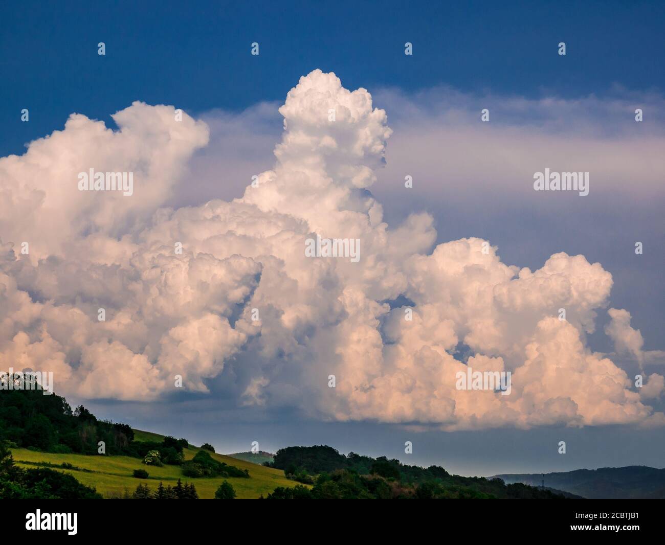 Enormi nuvole di pioggia - Cumulonimbus - che si formano in blu cielo su paesaggio collinare Foto Stock