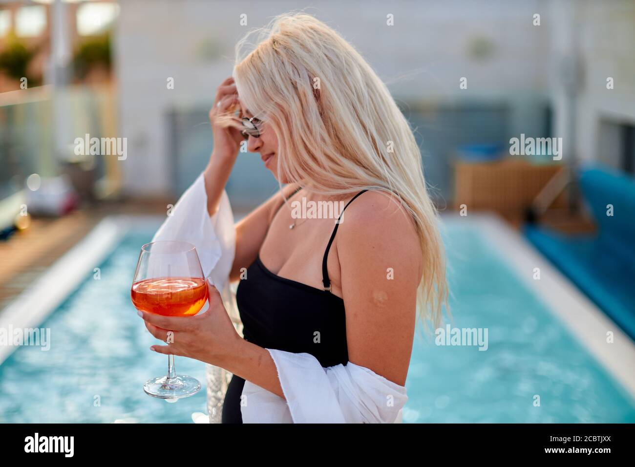 Bella, bionda viaggiatore donna in abito bianco spiaggia sta sorseggiando un cocktail in un bar sulla spiaggia durante il periodo estivo Foto Stock