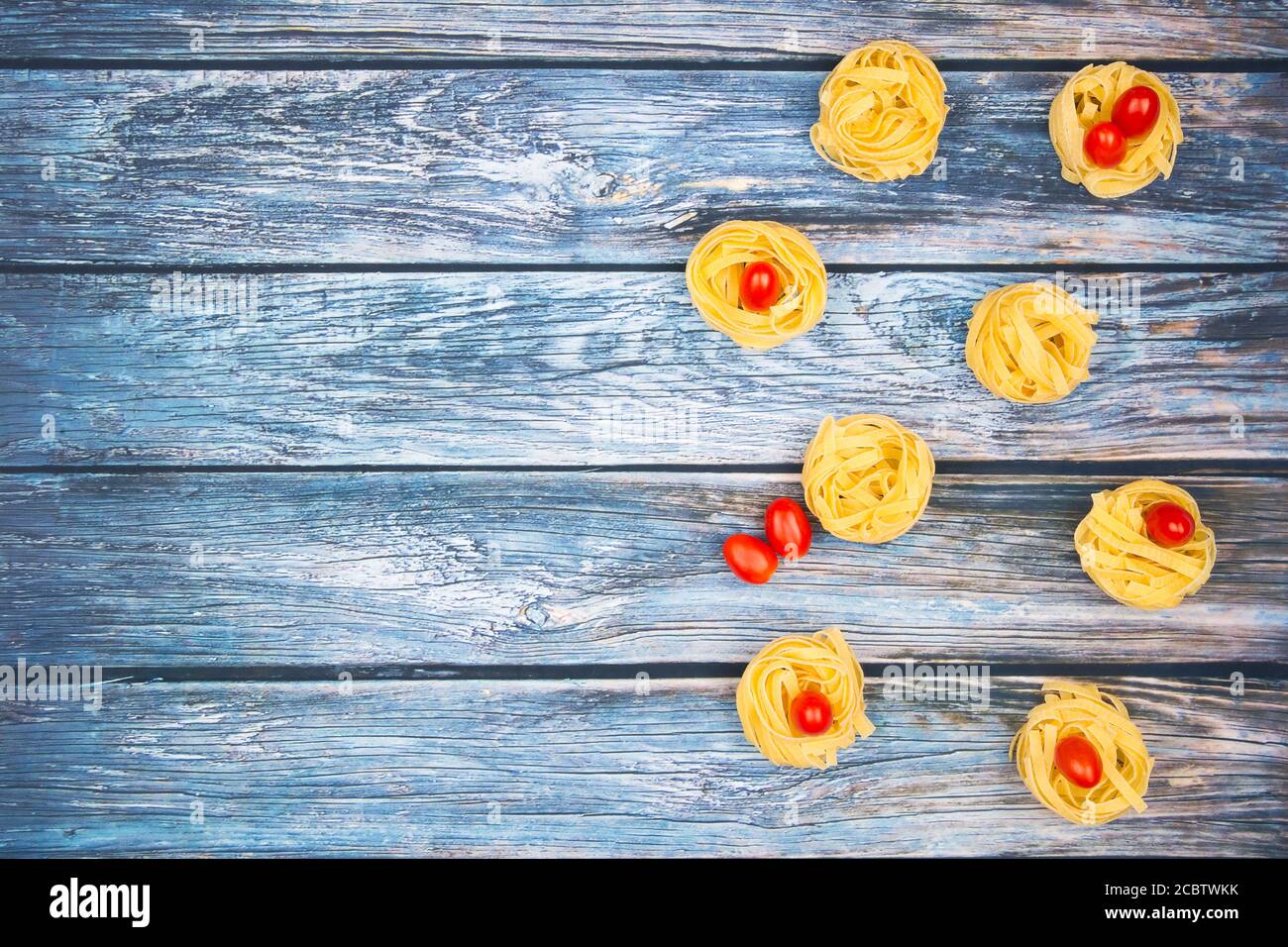 Primo piano di nidi di tagliatelle con pomodori roma mini a forma di uovo su un tavolo rustico in legno con burlap, Foto Stock