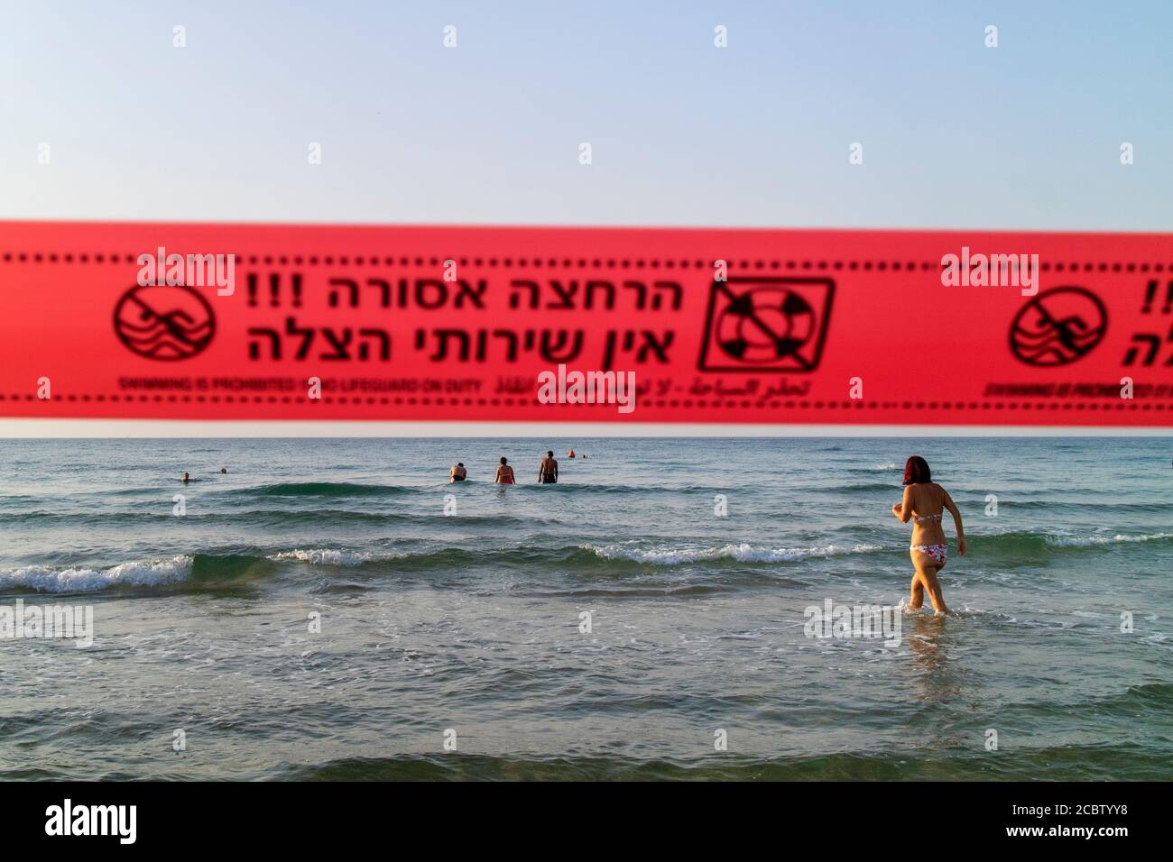 Persone che nuotano nell'oceano fuori Tel Aviv. Un nastro di avvertimento avverte che la pattuglia della spiaggia non è presidiata. Foto Stock