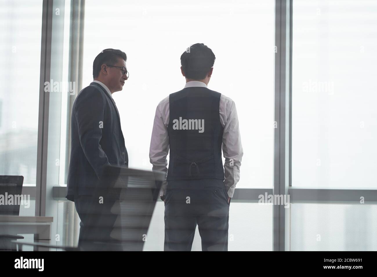 vista posteriore di due uomini d'affari asiatici che si trovano di fronte di finestra di ufficio che ha una discussione Foto Stock