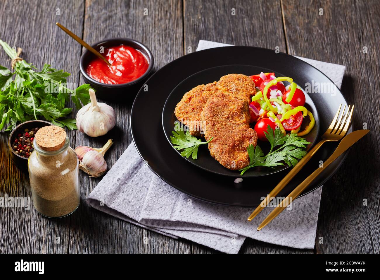 costolette di agnello impanate al forno servite con pomodoro, cipolla  rossa, insalata di pepe verde su un piatto nero su un tavolo di legno,  vista orizzontale, primo piano Foto stock - Alamy