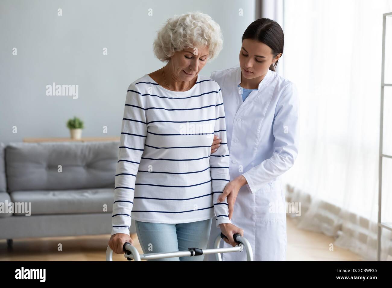 Giovane medico che aiuta i pazienti anziani disabili a camminare con telaio. Foto Stock