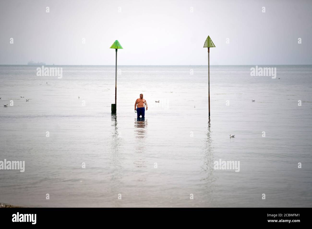 Un uomo si erge da solo in mare, come il tempo caldo a Southend, l'Essex continua. Foto Stock