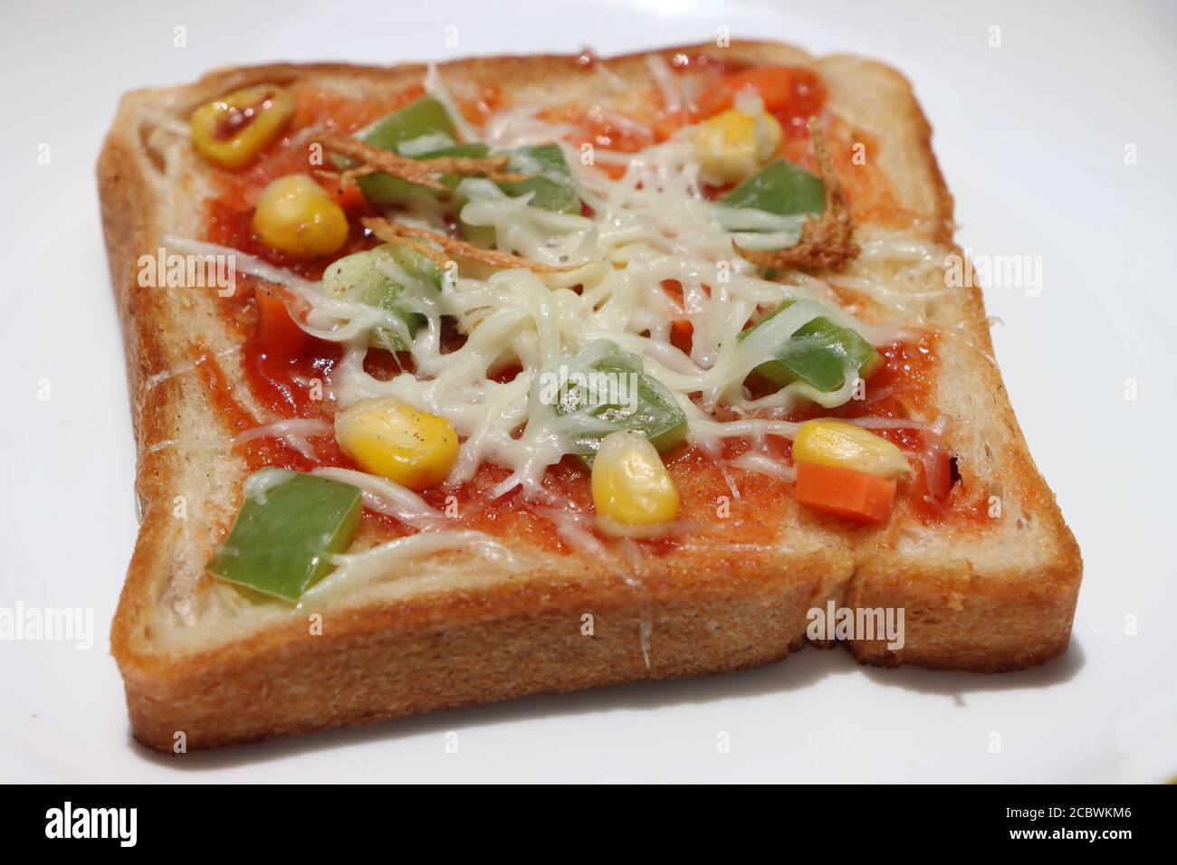 Pizza di pane marrone, condita con mais dolce, verdure e formaggio, colazione per bambini, cibo di strada indiano Foto Stock