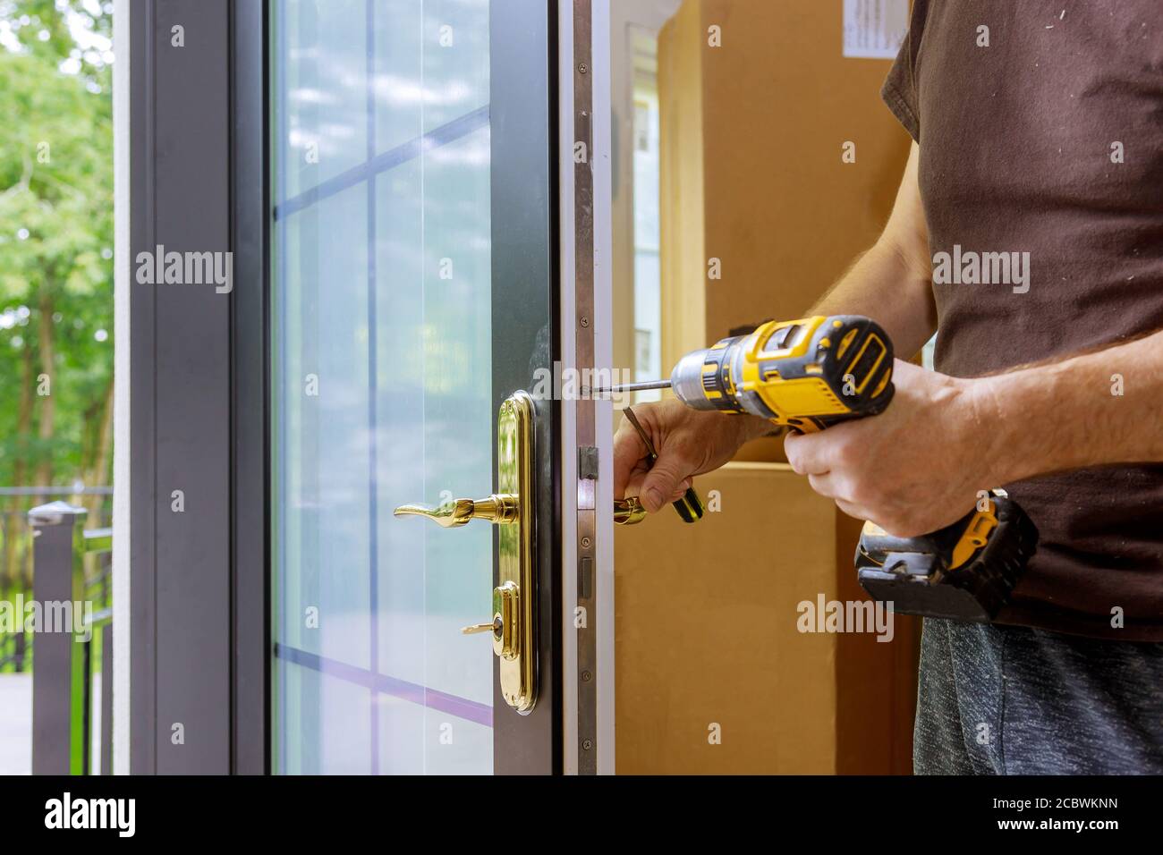 Installare la maniglia della porta con una serratura, falegname serrare la vite utilizzando un trapano elettrico cacciavite, close-up. Foto Stock