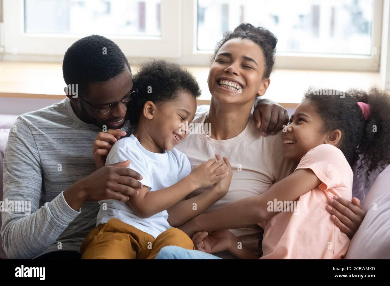 Affettuosi genitori neri che solleticano e ridono con i bambini a casa Foto Stock