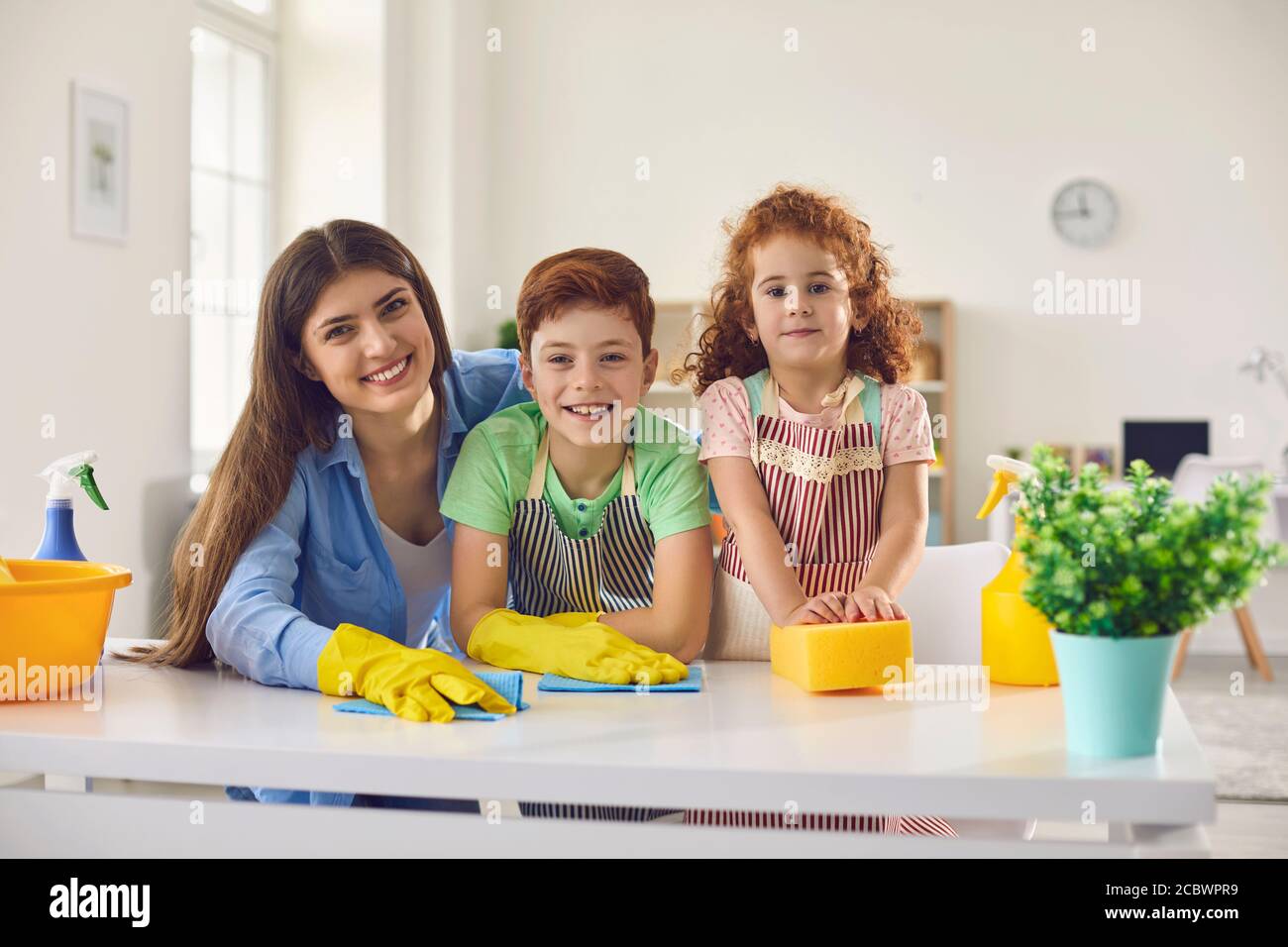 Buona famiglia con mamma e due bambini che si ripuliscono a casa. Genitori e bambini che fanno le faccende domestiche insieme all'interno Foto Stock