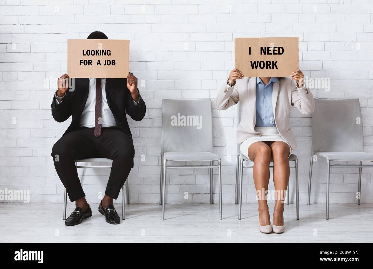 I candidati neri vacanti con i segni che HO BISOGNO DI LAVORO e DI GUARDARE PER LAVORO prima di un colloquio di lavoro nel foyer dell'ufficio Foto Stock