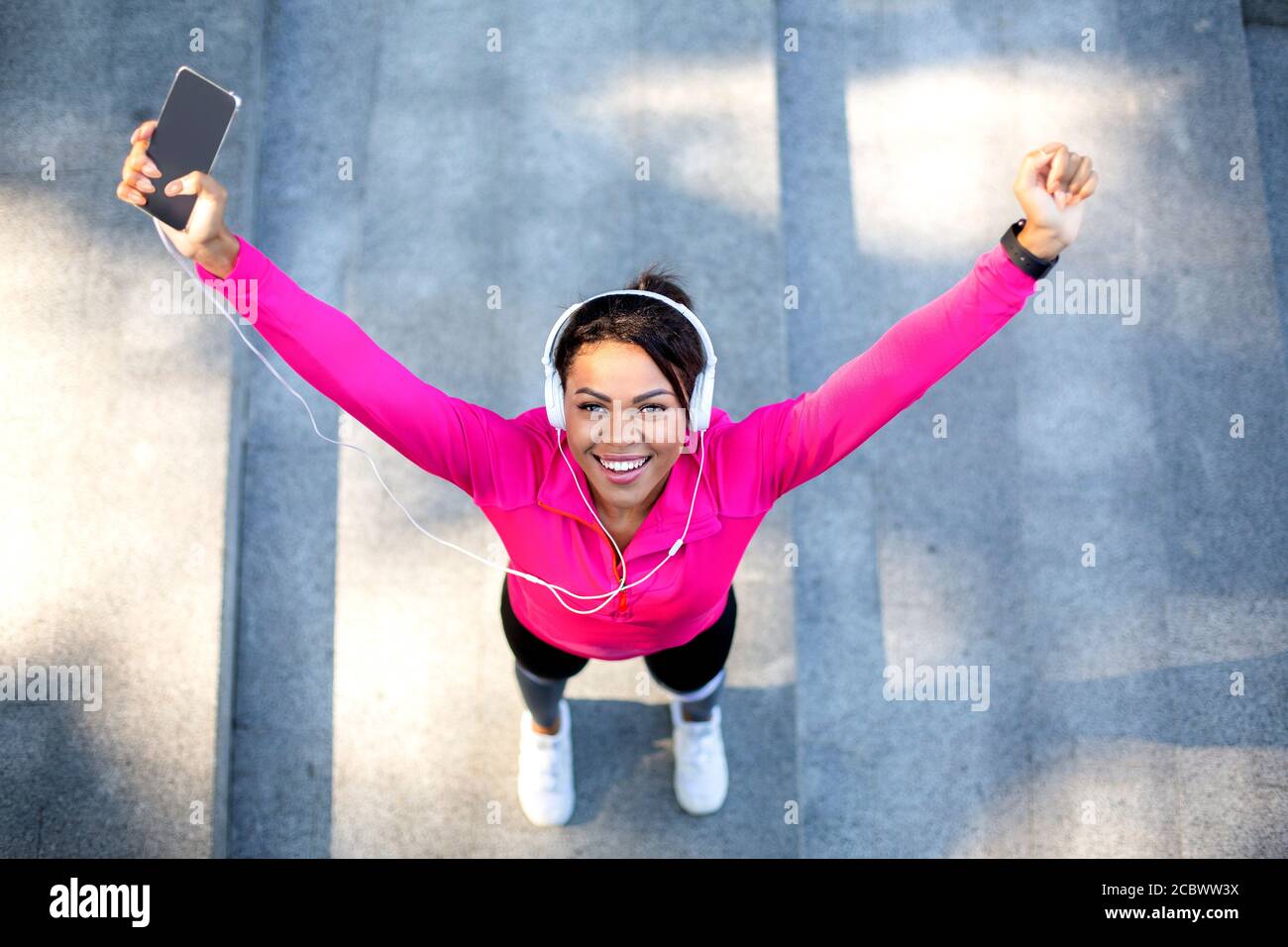 Vista dall'alto del gioioso jogger nero che tiene lo smartphone Foto Stock