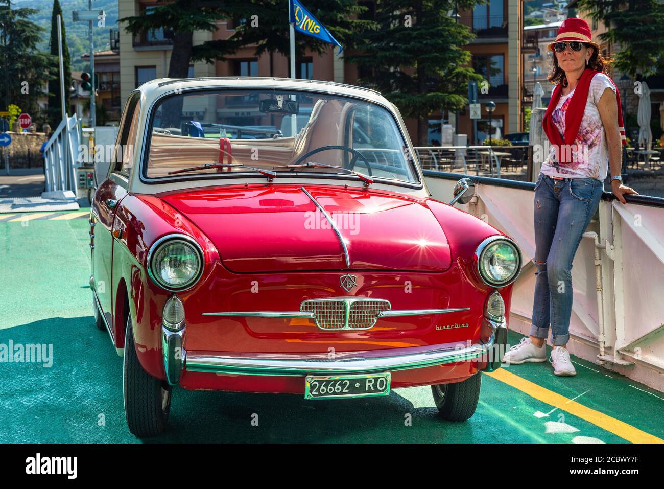 Una donna si trova accanto ad una classica Autobianchi Bianchina Trasformabile rossa sul ponte di un traghetto sul Lago di Garda Foto Stock