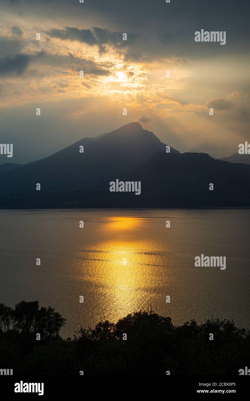 Il sole serale splende attraverso le nuvole di tuono sul Monte Pizzocolo e sul lago di Garda, in Italia Foto Stock