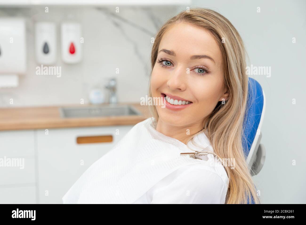 Giovane donna sorridente seduta sulla sedia presso l'ufficio dentista. Cura dentale, denti sani. Foto Stock