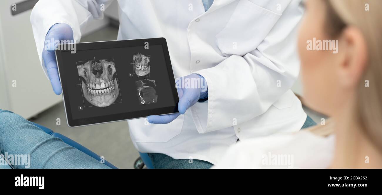 Consulenza dentale in clinica. Dentista che mostra i raggi X dei denti sullo schermo del tablet digitale. Tecnologia di tomografia 3D. Foto Stock