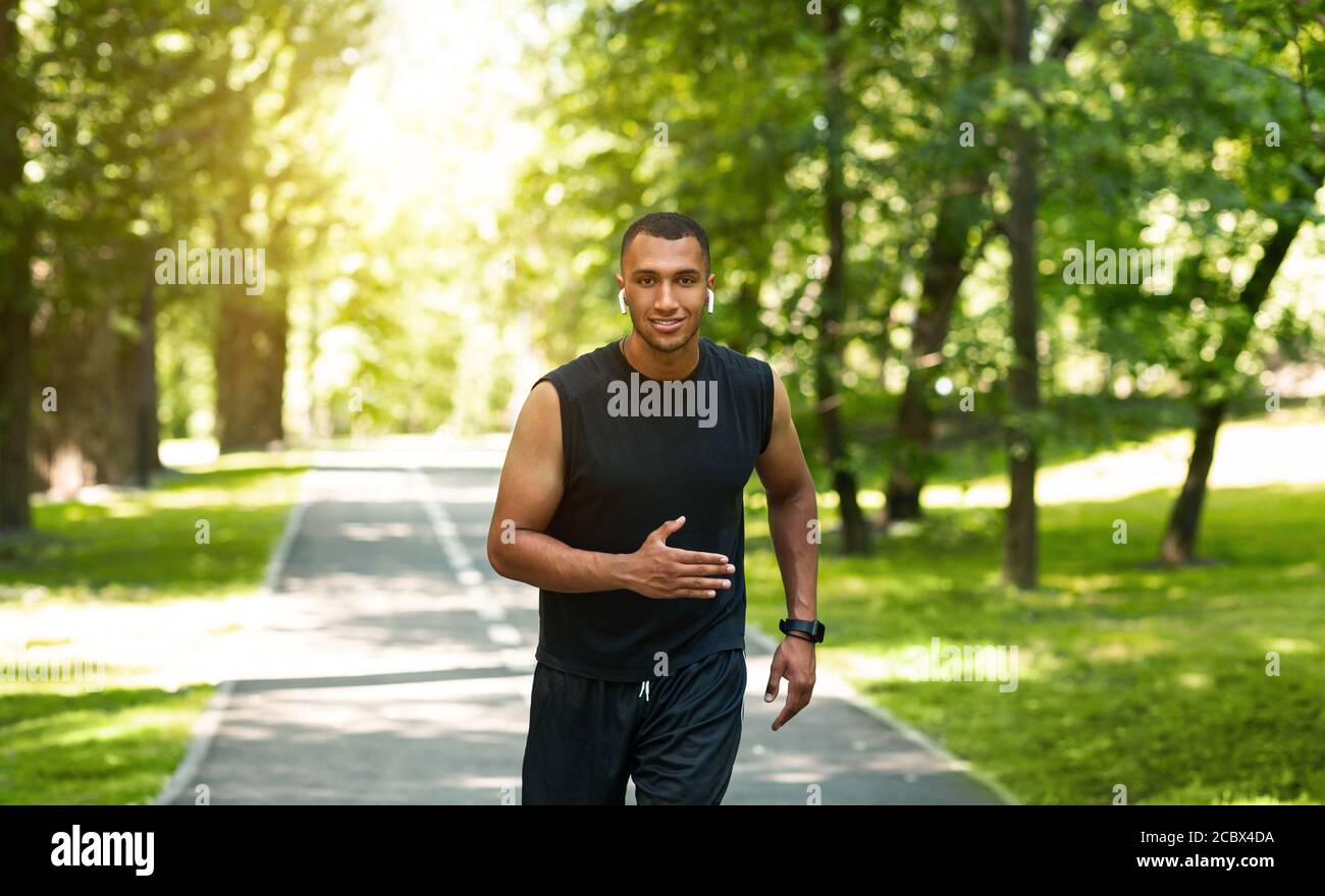 Felice corridore afroamericano jogging al parco cittadino su soleggiato giorno Foto Stock