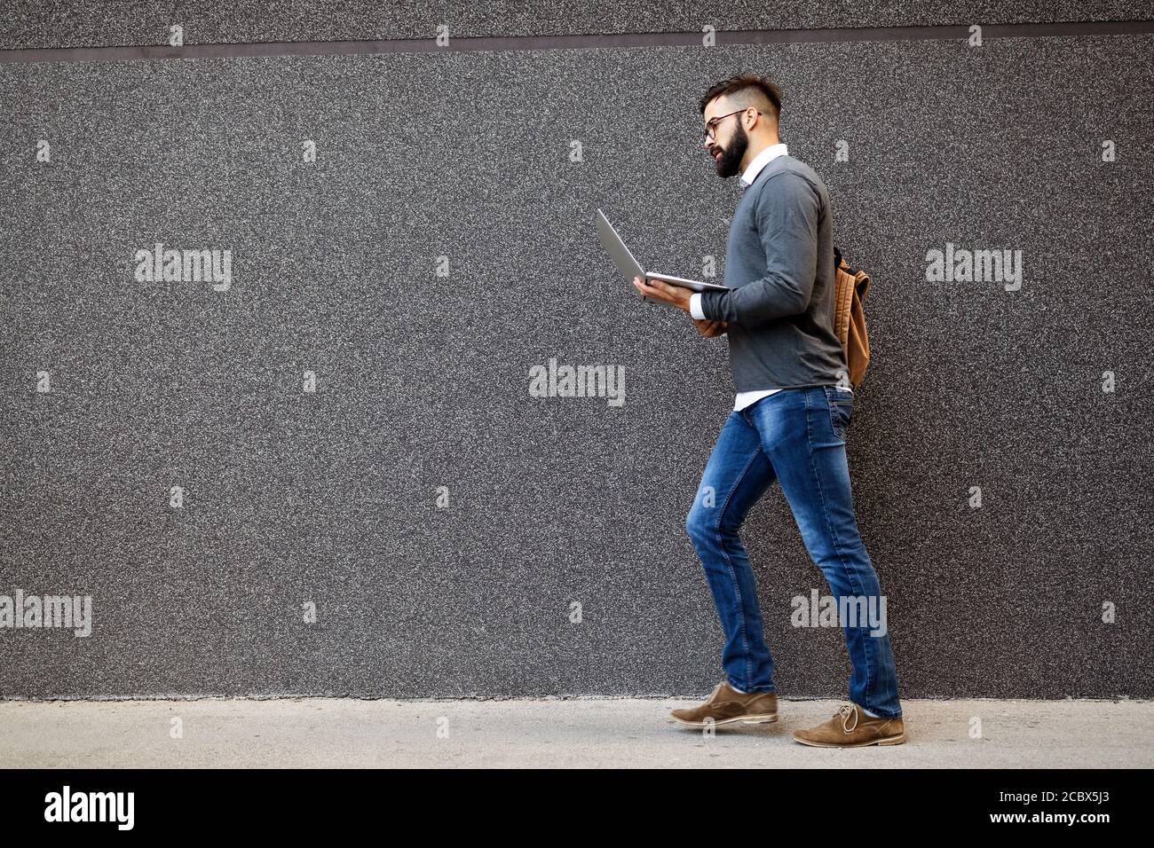 Uomo d'affari a piedi in strada tenendo il suo portatile, lavorando all'aperto Foto Stock