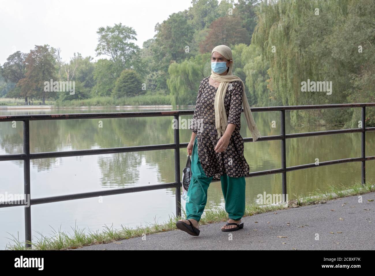 Una donna musulmana che indossa un copricapo e una maschera chirurgica cammina lungo il lago nel Kissena Park, Flushing, New York City Foto Stock