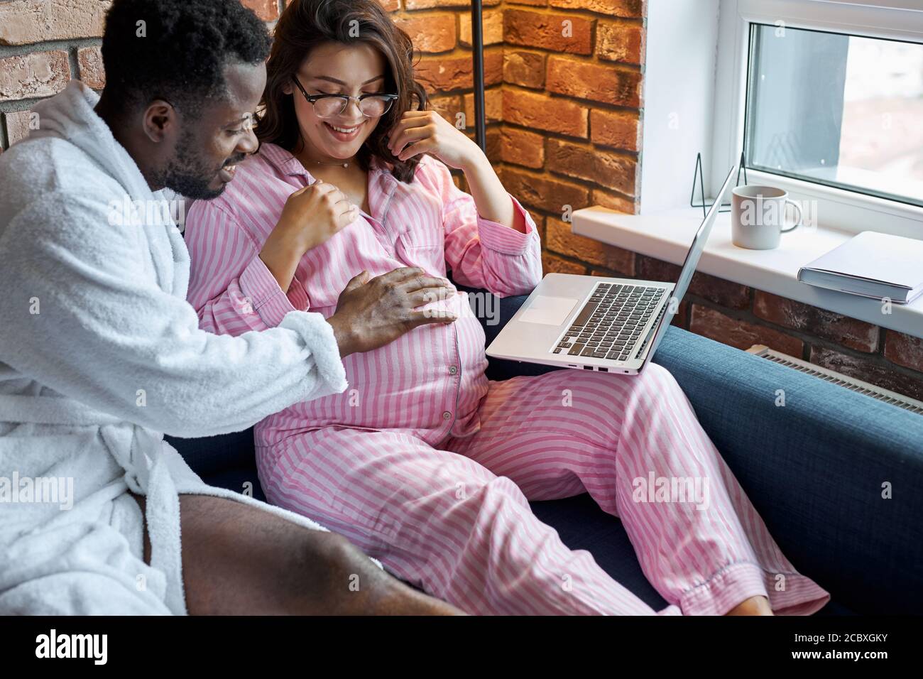 bell'uomo africano colpo la moglie incinta tummy mentre lei è seduta con il laptop, l'amore e il concetto di bambino in attesa Foto Stock