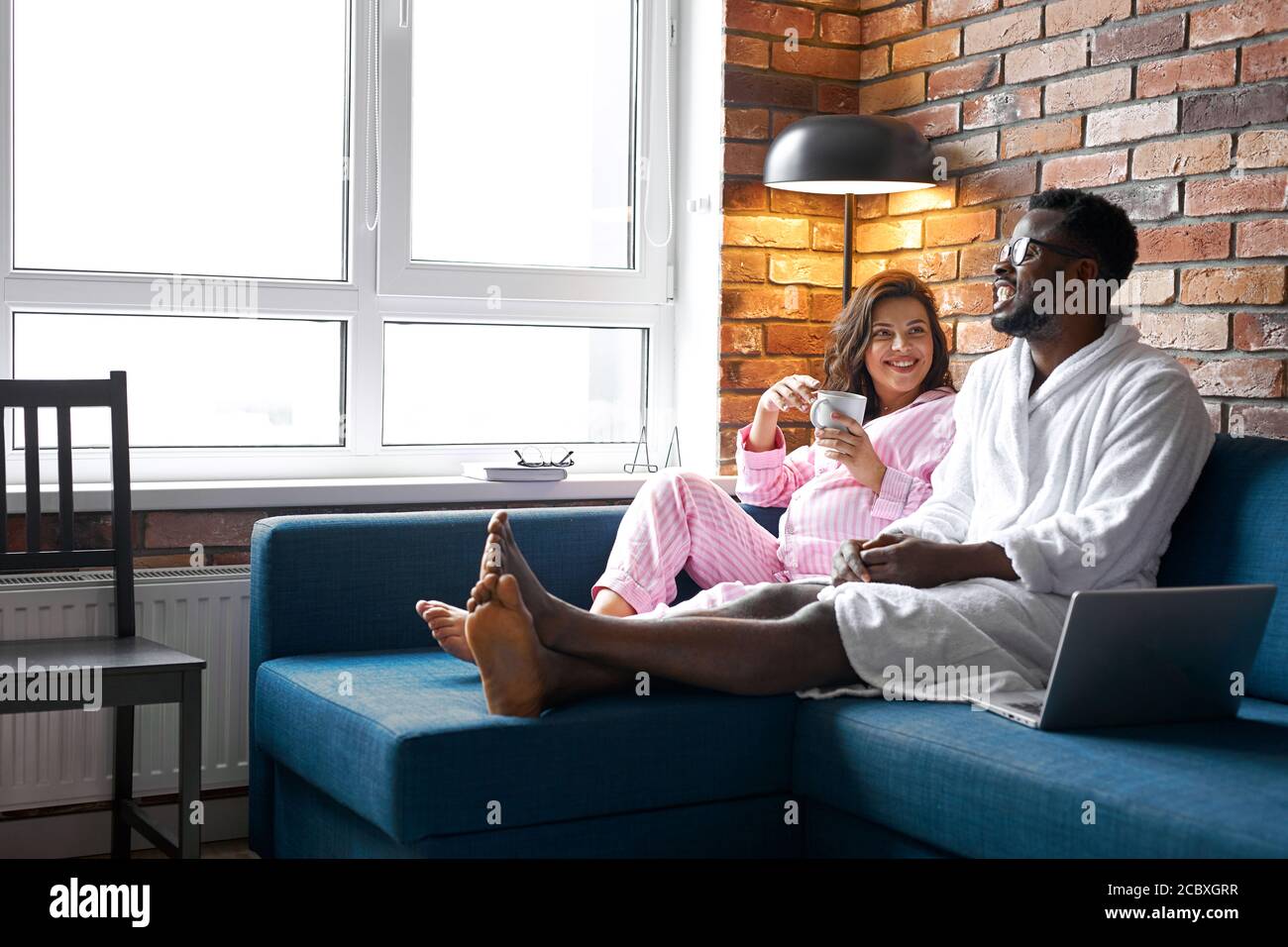 famiglia multietnica felice hanno riposo, parlare a casa, tempo libero. marito e moglie incinta in camera moderna interni. il concetto di gravidanza, riposo ed ex Foto Stock